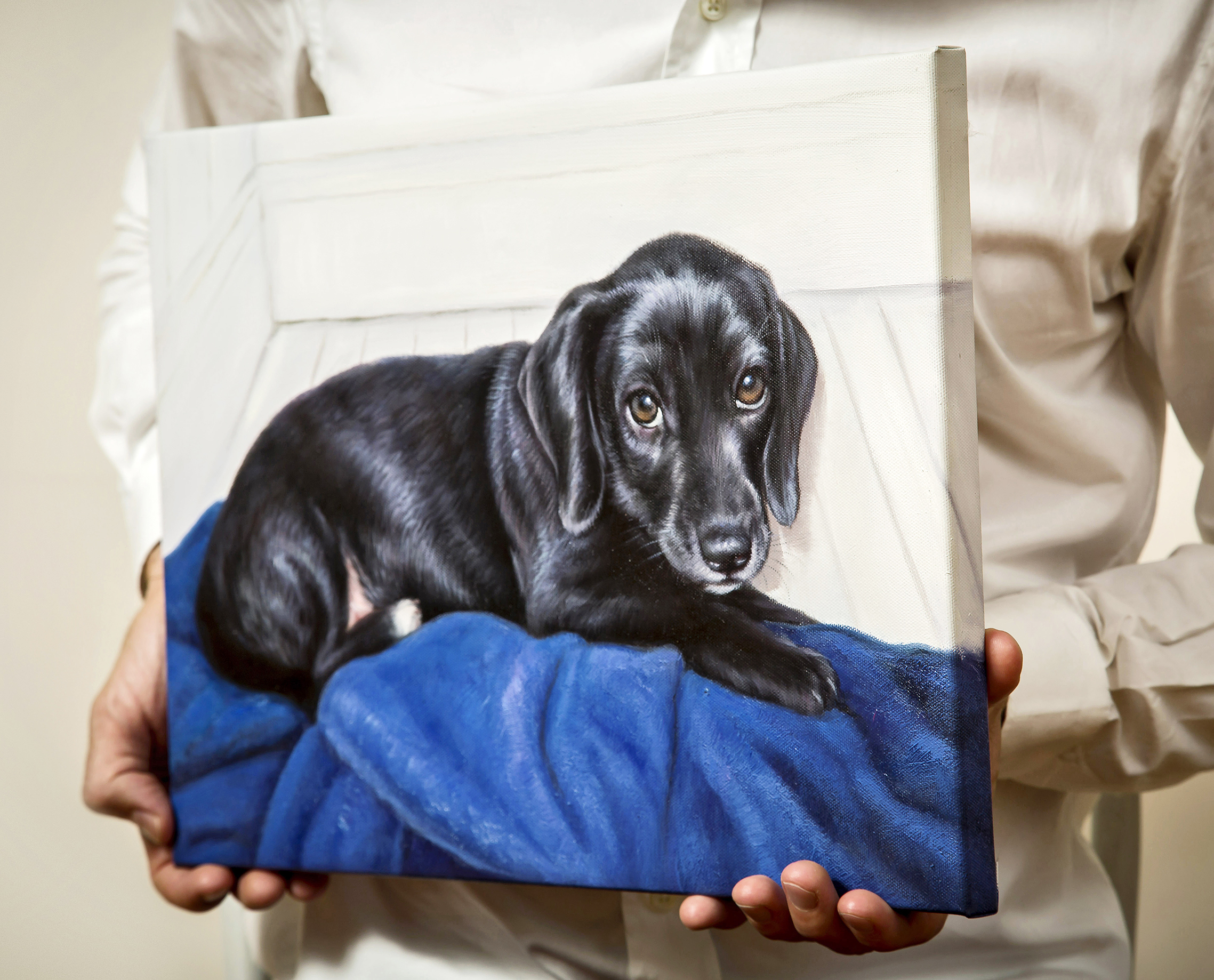 A pair of hands holding an oil painting of a black puppy